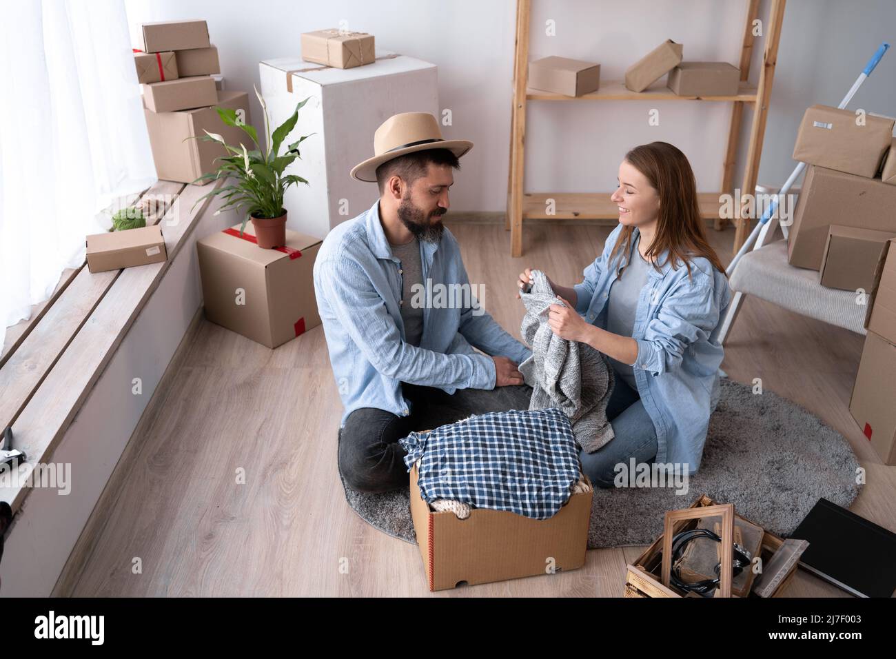 Ein Mann und eine Frau sitzen am Tag der Bewegung auf dem Boden und packen die Sachen aus. Glückliches Paar in einer neuen Wohnung. Das Konzept der Vermietung und Kauf eines Hauses Stockfoto