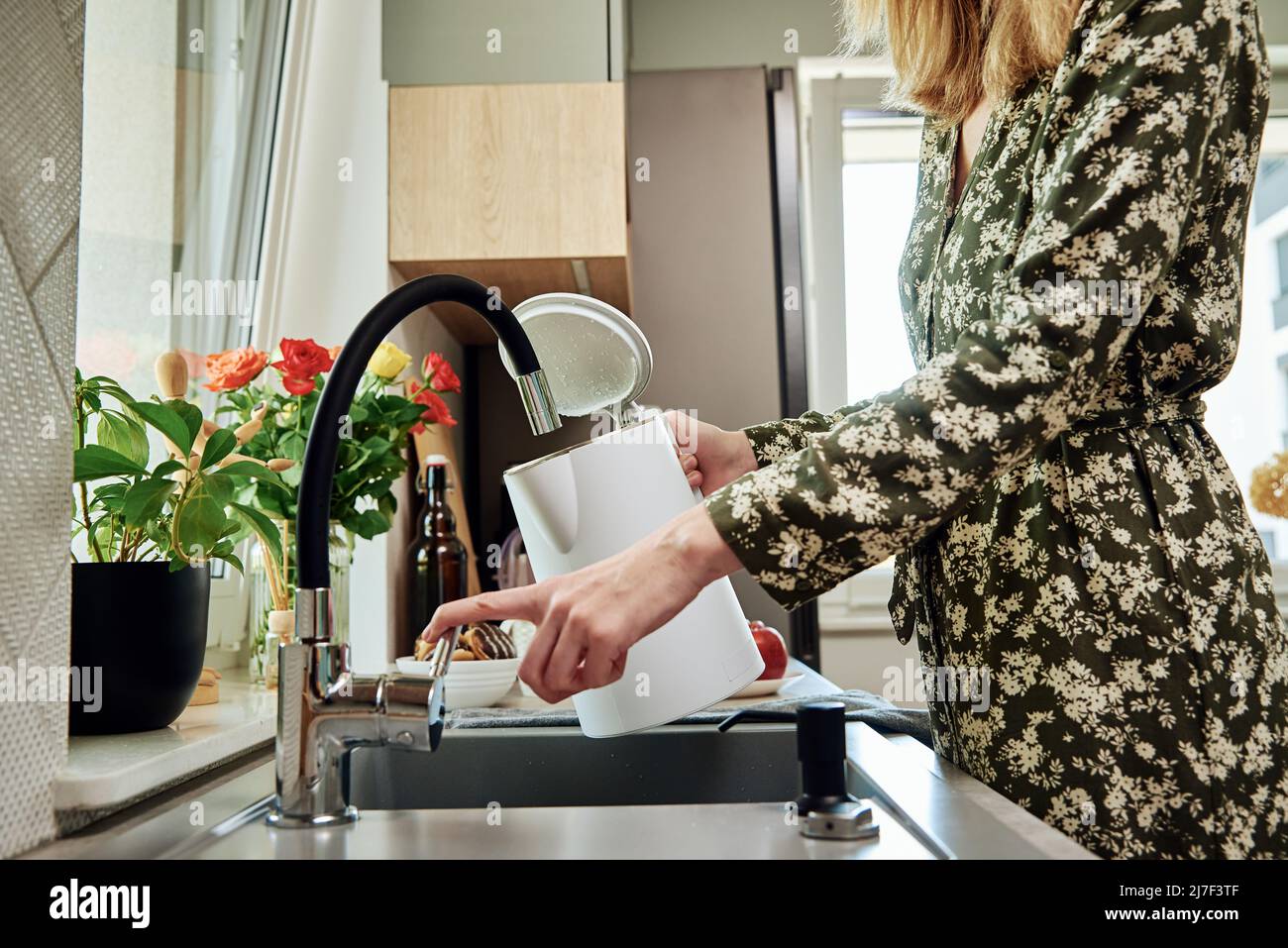 Frau gießt sauberes gefiltertes Wasser aus dem Wasserhahn in den Wasserkocher, um Wasser in der Küche zu kochen Stockfoto