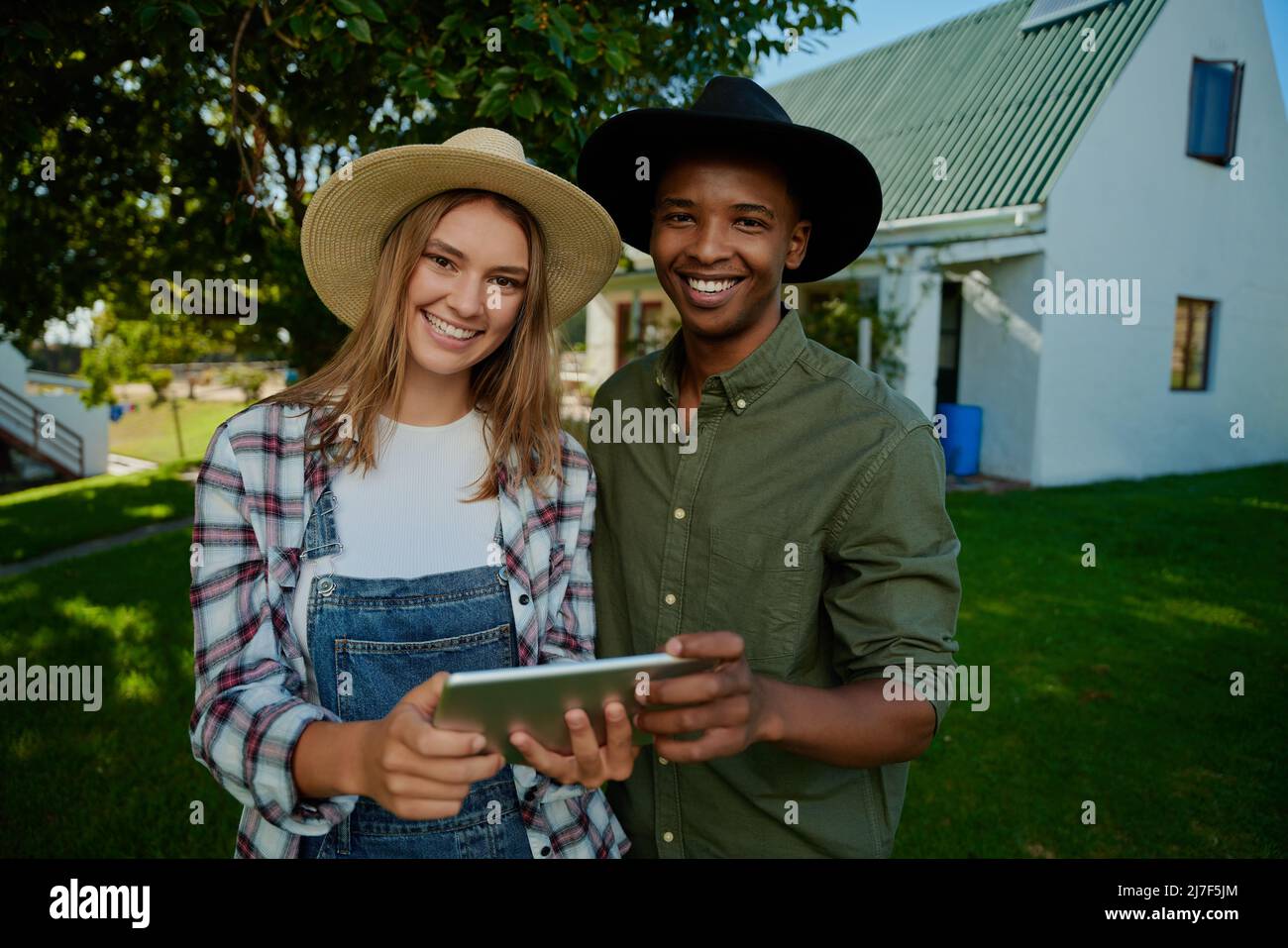Bauern mit gemischter Rasse stehen im Freien und lächeln, während sie ein digitales Tablet halten Stockfoto