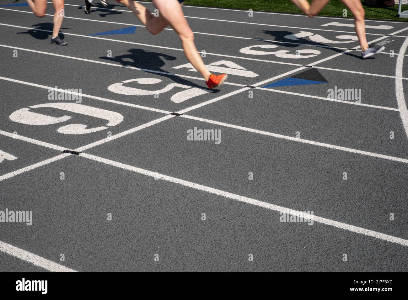 Auf einer grauen Strecke mit nummerierten Bahnen und einer Ziellinie mit Kopierfläche laufen die Outdoor- und Feldrennstrecken. Zwei Läufer überqueren die Linie. Stockfoto
