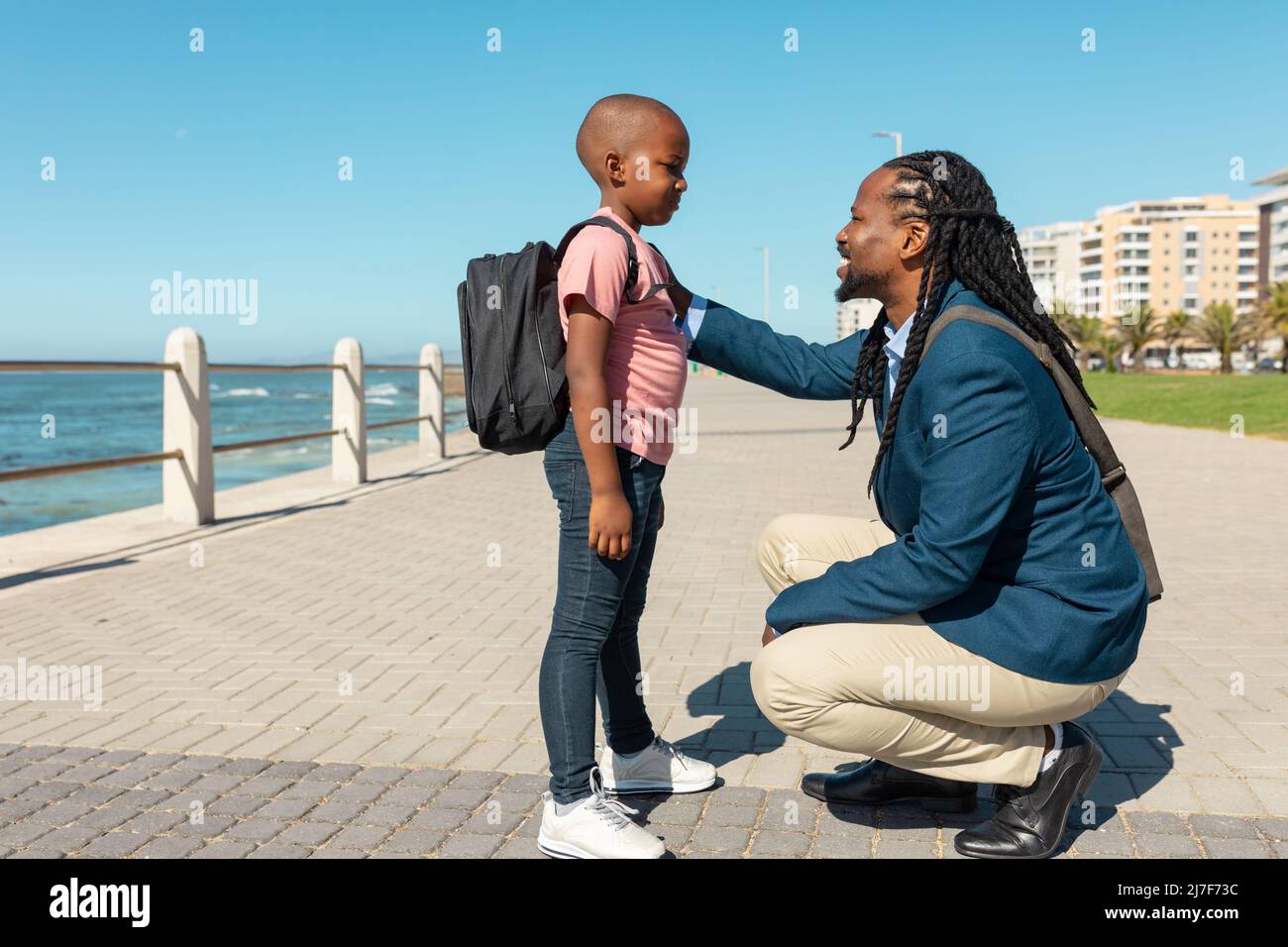Lächelnder afroamerikanischer Vater hockend, während er mit dem Sohn an der Promenade mit der Hand auf der Schulter sprach Stockfoto