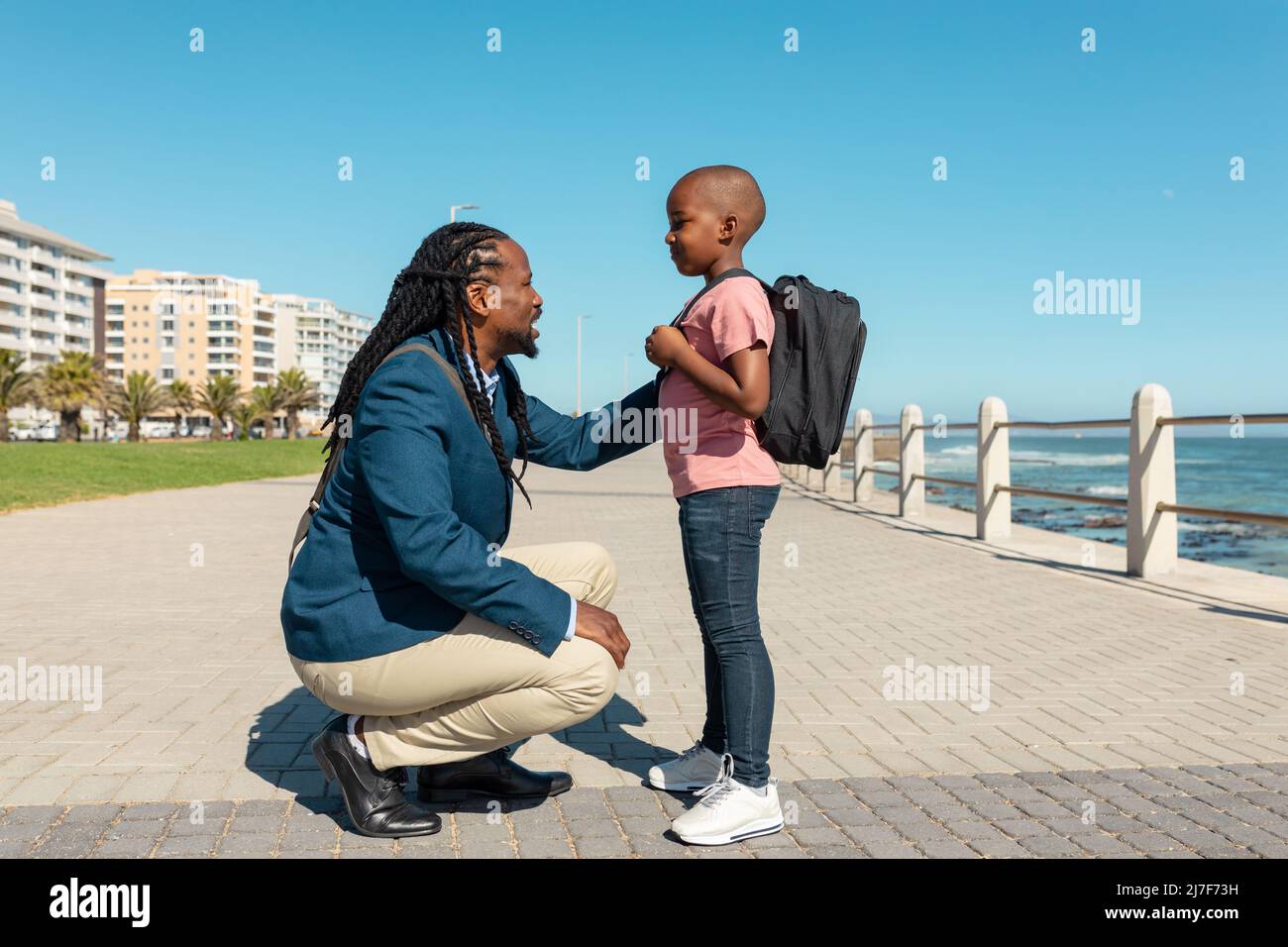 afroamerikanischer Vater hockend, während er mit dem Sohn mit der Hand auf der Schulter an der Promenade sprach Stockfoto
