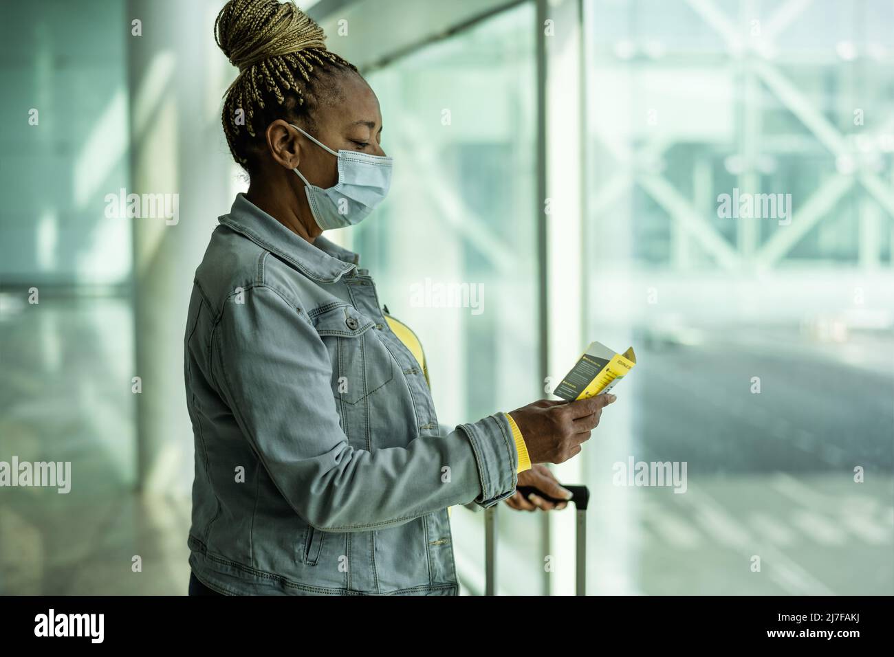 Afrikanische ältere Frau im Flughafenterminal mit Gepäck, das während einer Coronavirus-Pandemie eine Gesichtsmaske trug Stockfoto