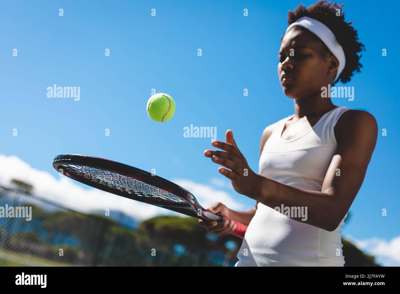 Junge afroamerikanische Tennisspielerin spielt mit Schläger und Ball auf dem Platz gegen den Himmel Stockfoto