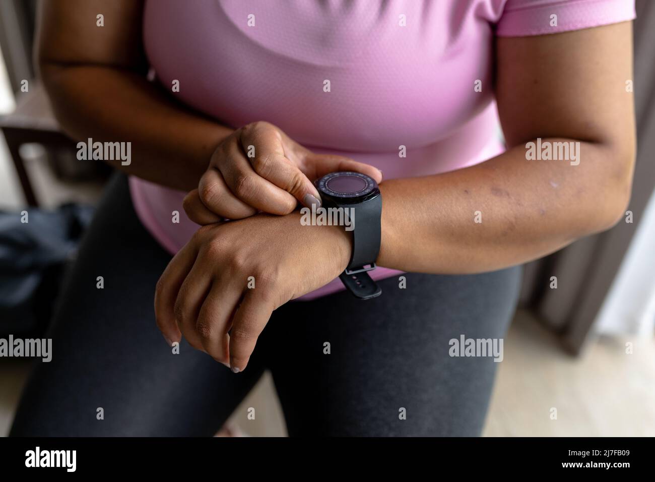 Mittelteil einer afroamerikanischen Frau mit mittlerem Erwachsenen, die die Zeit überprüft, während sie zu Hause sitzt Stockfoto