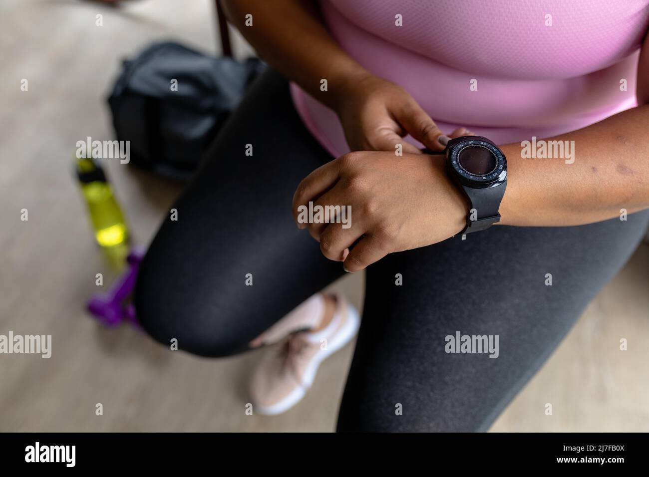 Unterer Teil einer afroamerikanischen Frau mit mittlerem Erwachsenen, die eine Armbanduhr trägt, während sie zu Hause sitzt Stockfoto