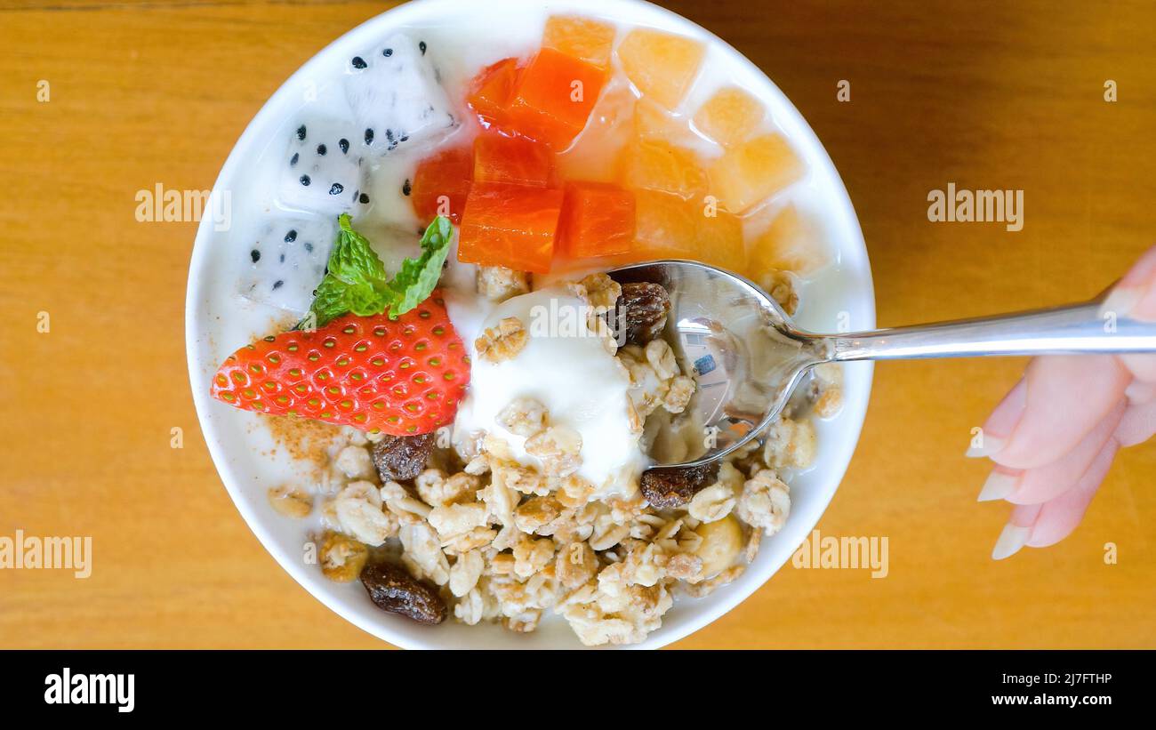 Frau Hand mit Löffel essen Schüssel mit hausgemachtem Müsli mit Joghurt und frischen Beeren Stockfoto