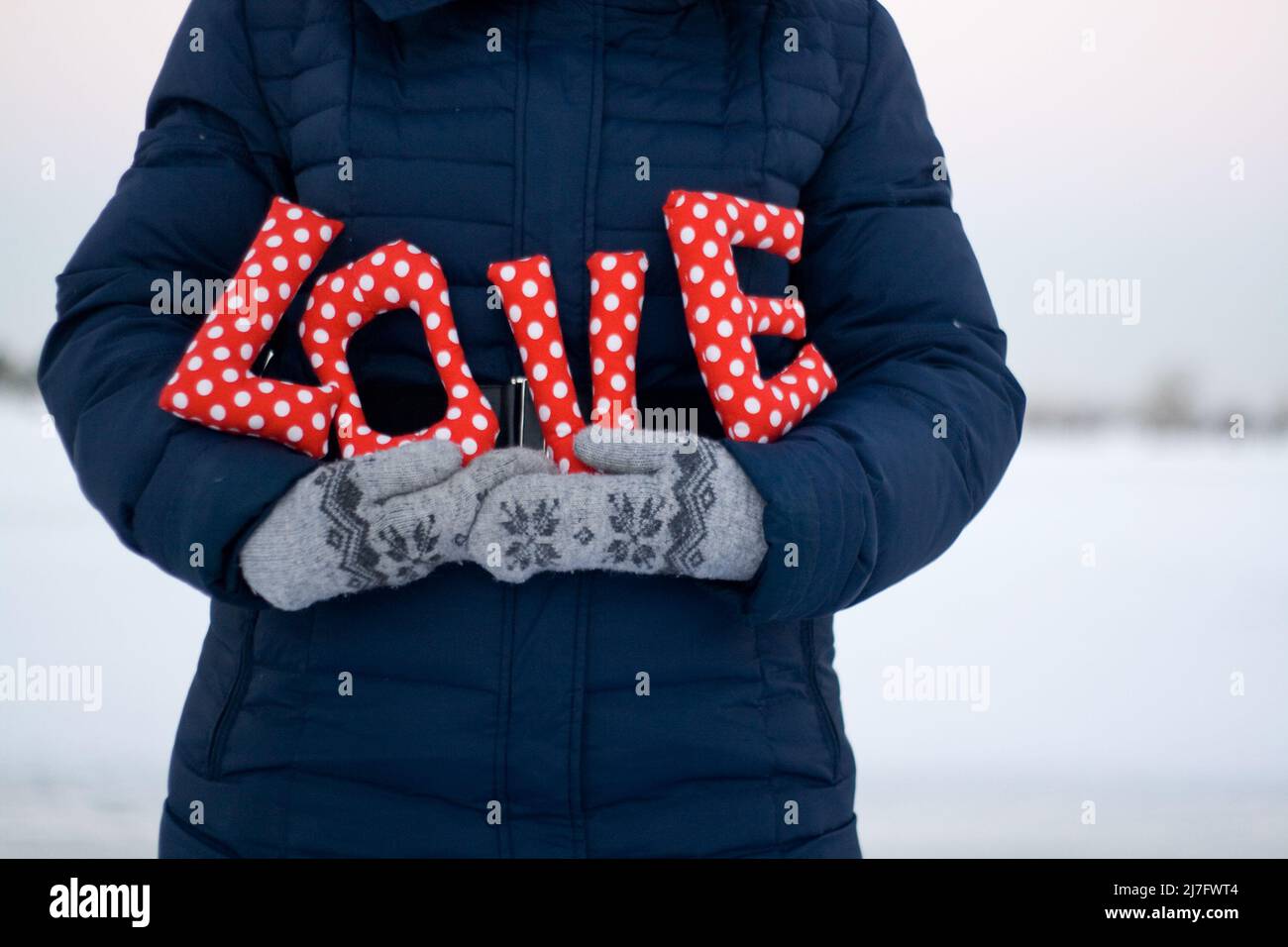Mädchen in blauer Daunenjacke und Handschuhen mit einem Schild „Love“ Stockfoto