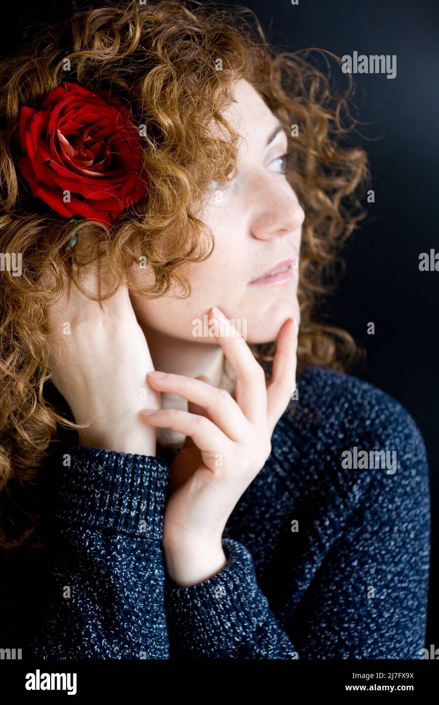 Porträt einer schönen jungen Rotschopf mit lockigen roten Rose in den Haaren auf einem dunklen Hintergrund Stockfoto