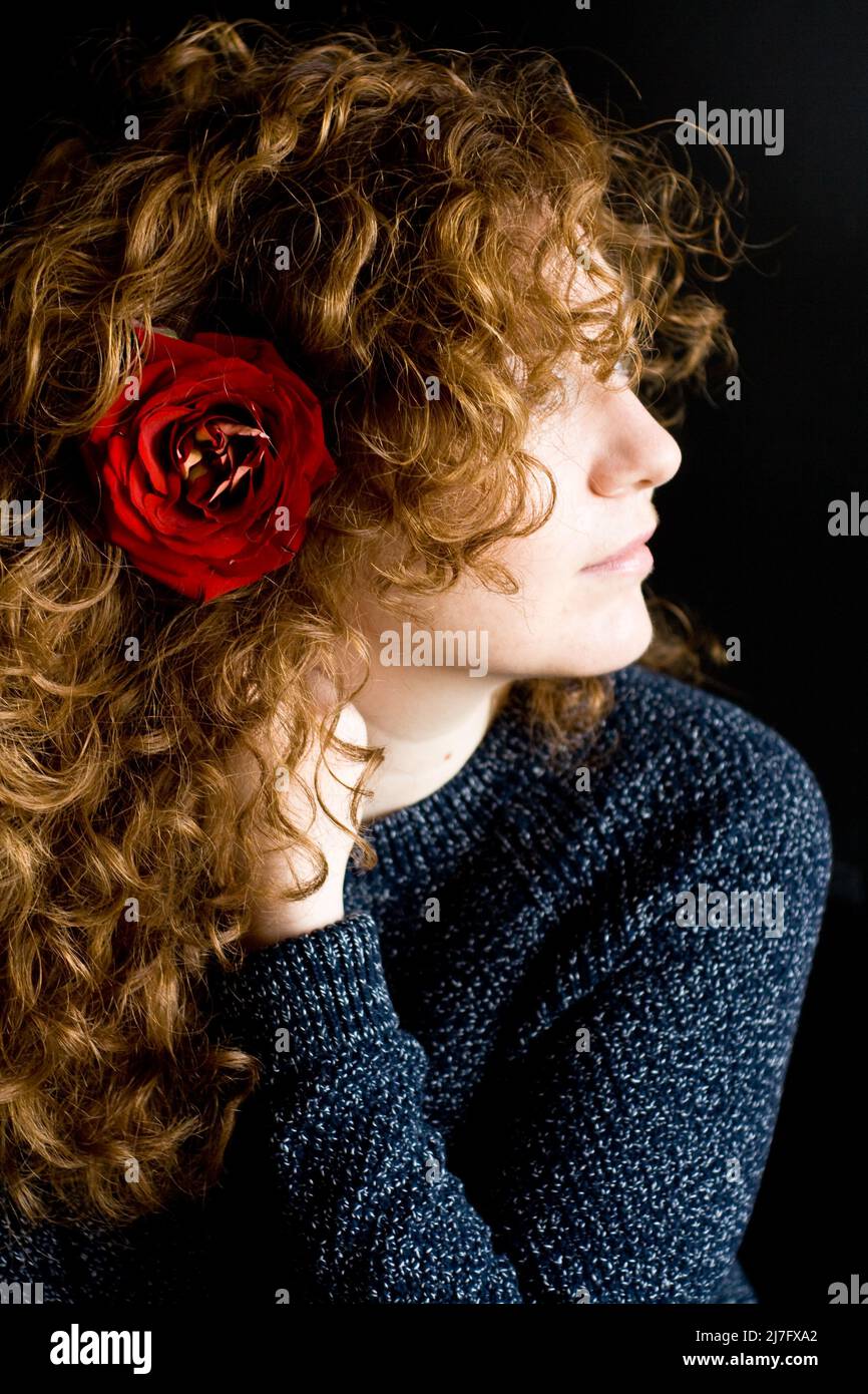 Porträt einer schönen jungen Rotschopf mit lockigen roten Rose in den Haaren auf einem dunklen Hintergrund Stockfoto