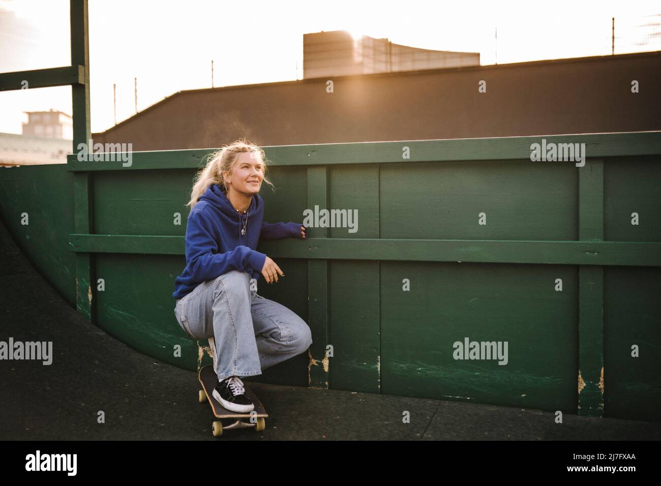 Lächelndes Teenager-Mädchen, das auf dem Skateboard hockend ist Stockfoto