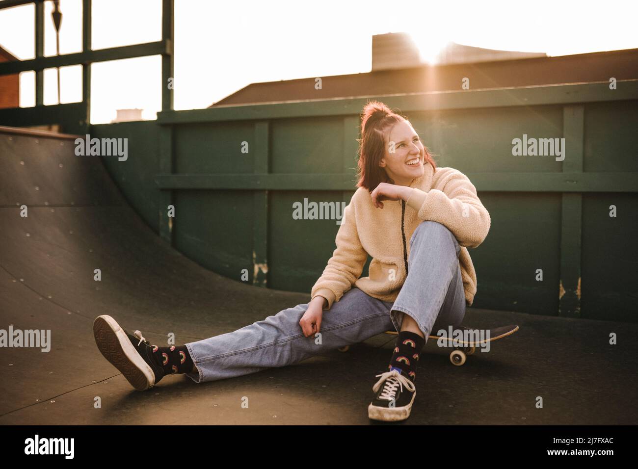 Lächelndes Teenager-Mädchen, das auf dem Skateboard sitzt Stockfoto
