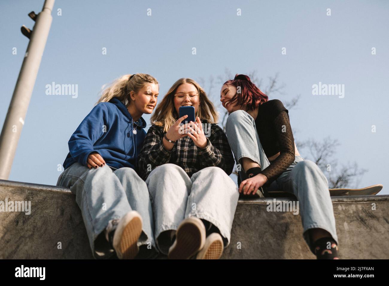 Lächelnde Teenager-Mädchen, die im Skatepark Smartphone benutzen Stockfoto