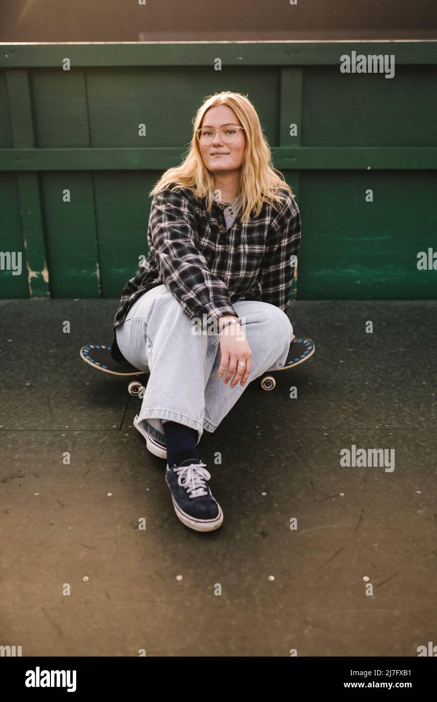 Porträt von lächelnden Teenager-Mädchen auf Skateboard sitzen Stockfoto