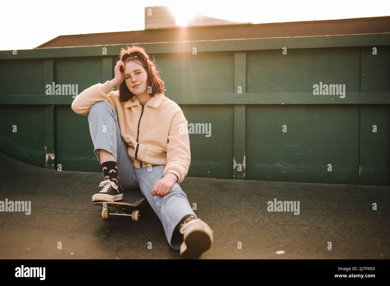 Porträt eines Teenagers, das auf dem Skateboard sitzt Stockfoto
