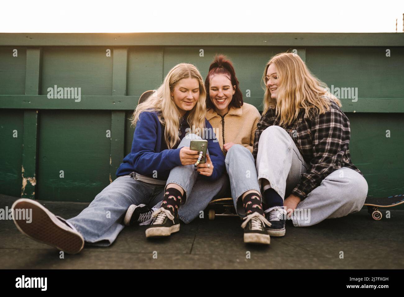 Teenager-Mädchen sitzen auf Skateboards und mit Smartphone Stockfoto