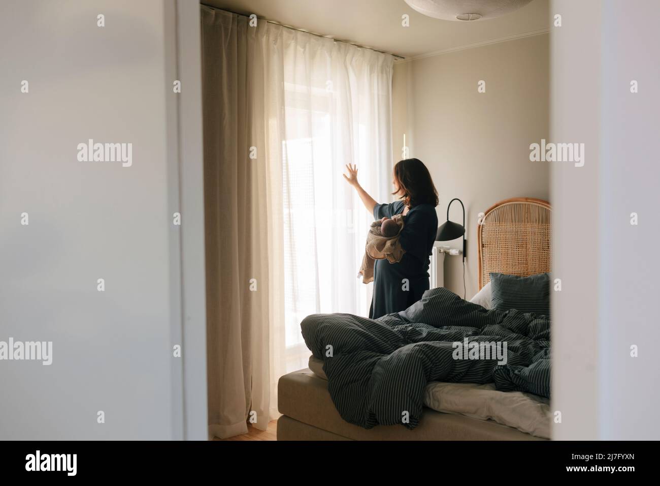 Modern hält Neugeborenes und schaut durch das Fenster Stockfoto