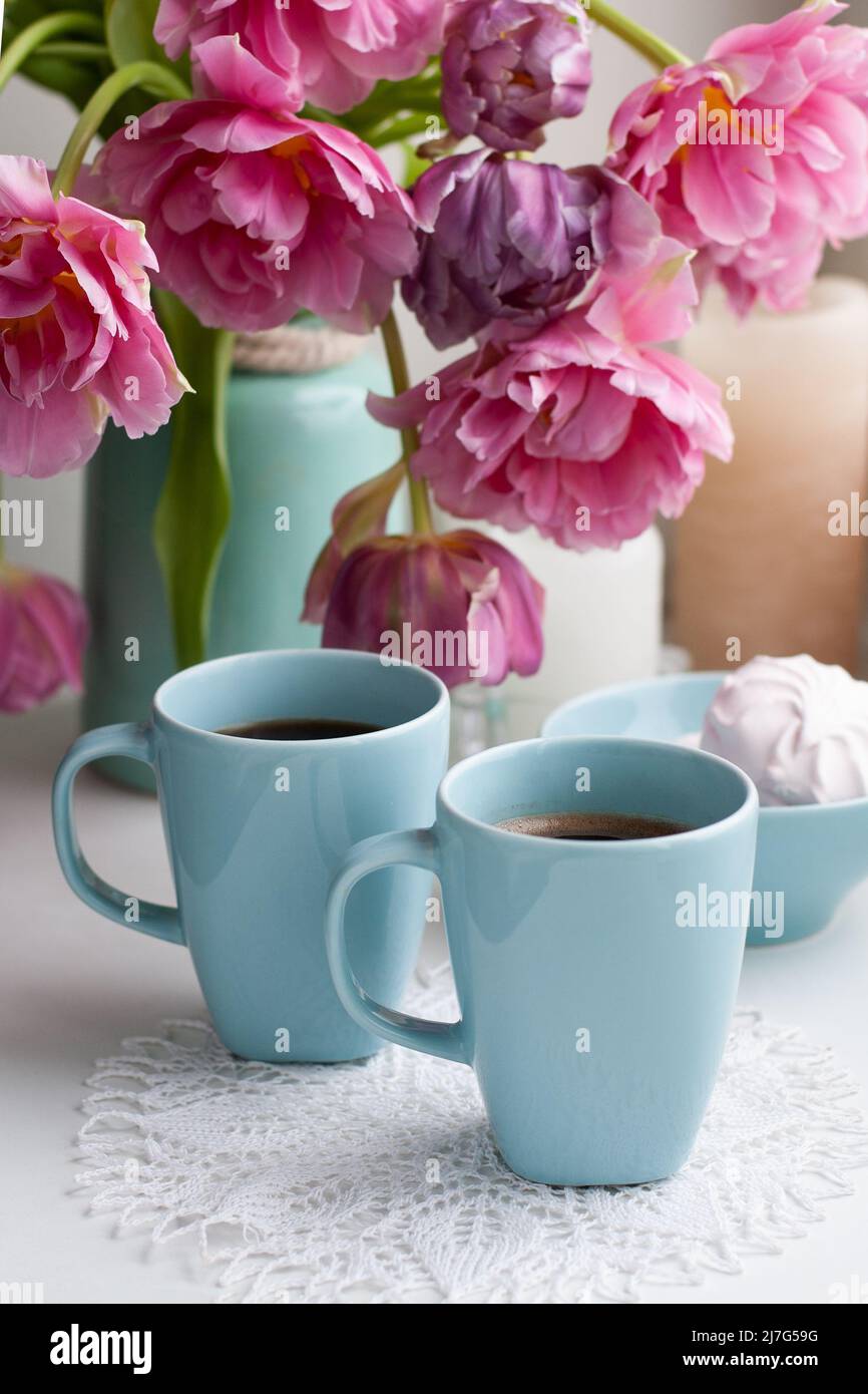 Zwei Tassen schwarzen Kaffee und ein zartes Marschlauch zum Frühstück stehen neben einem schönen Bouquet aus rosa Tulpen in einer blauen Vase. Stockfoto