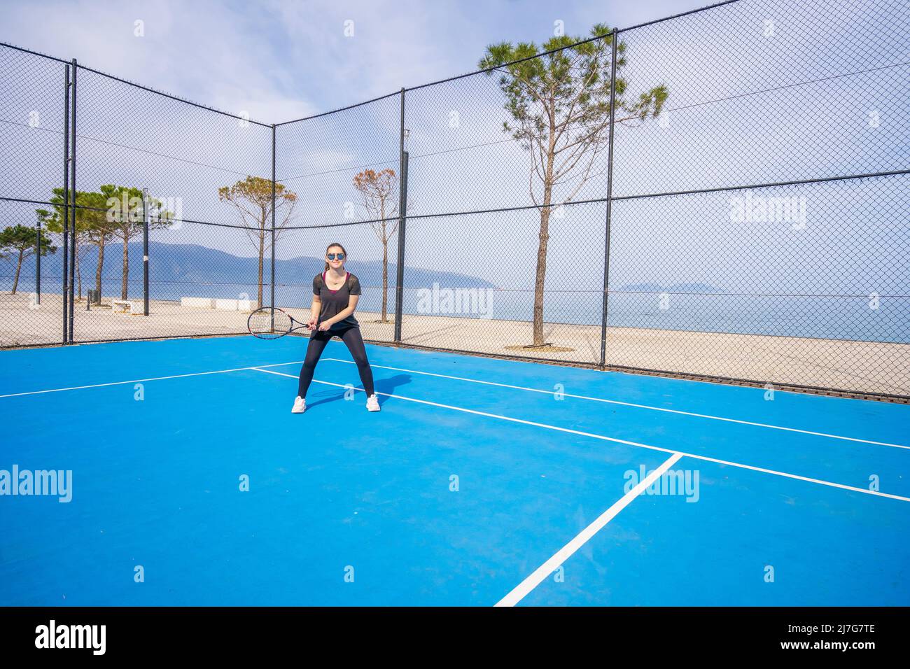 Das junge Mädchen in einem dunkelblauen Kleid spielt Tennis auf dem Platz mit einer harten blauen Beschichtung Stockfoto