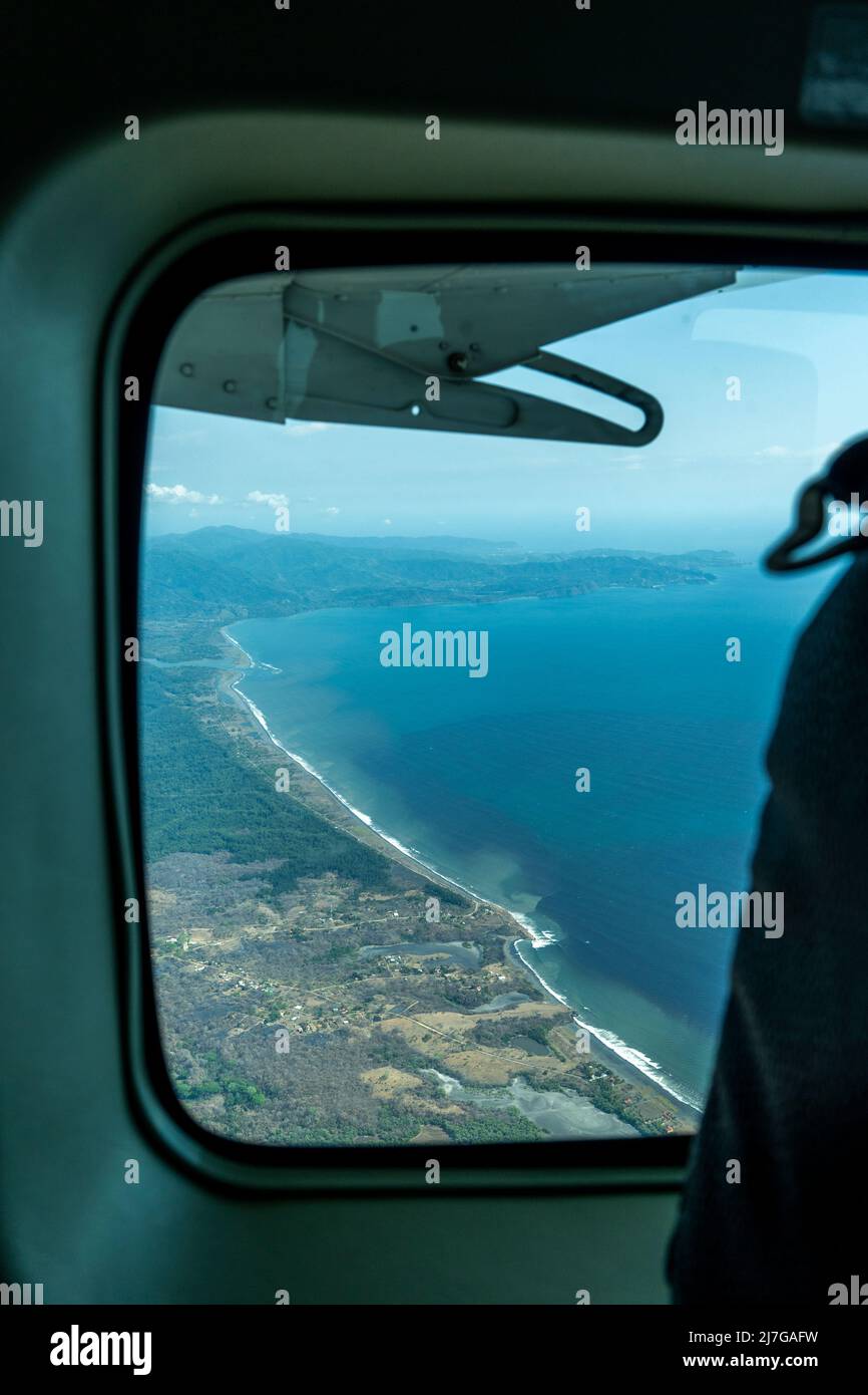 Bullauge aus dem Flugzeug mit Blick auf die Küste, den Strand und das Meer vom Innensitz aus Stockfoto
