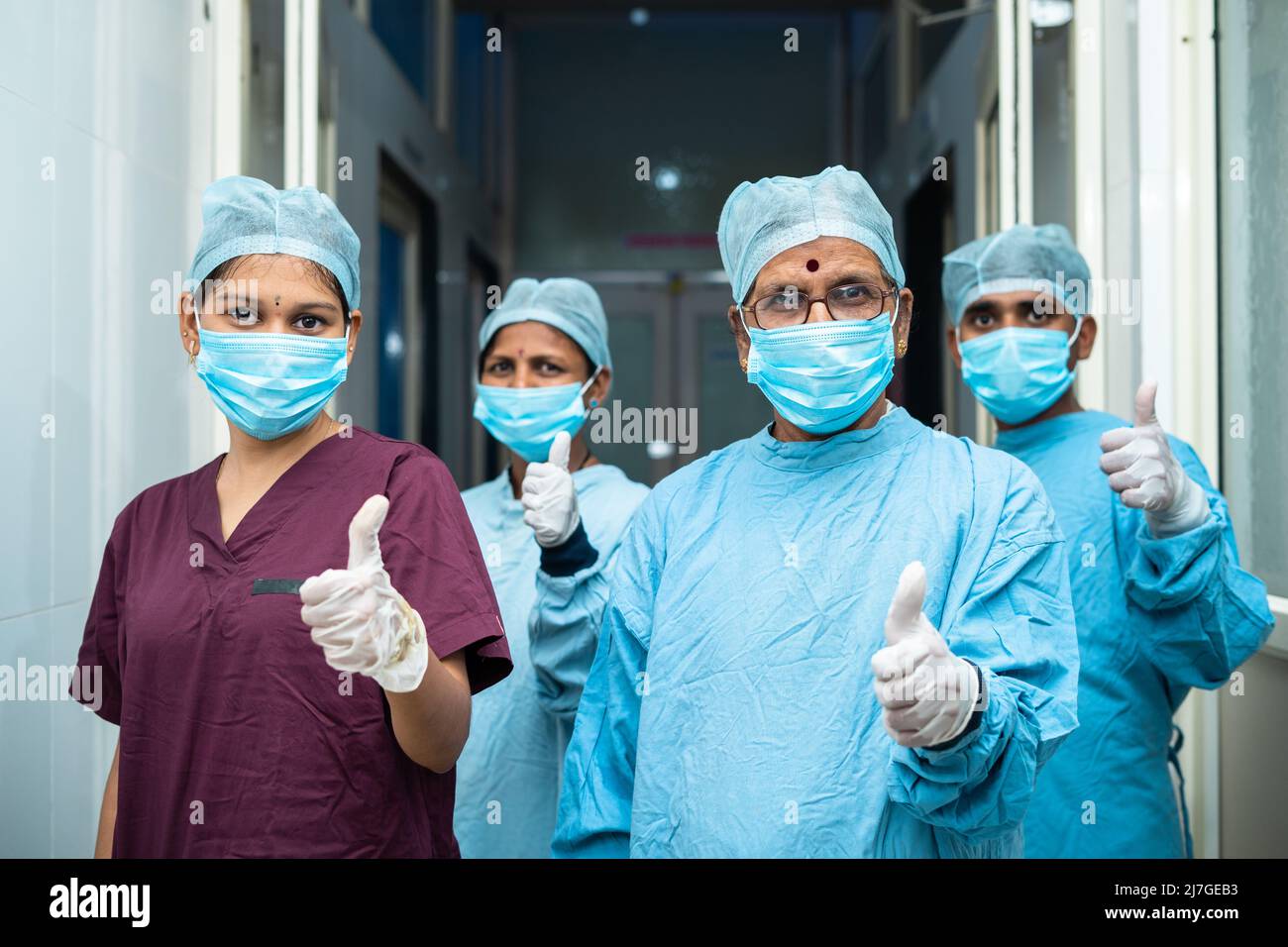 Gruppe von Chirurgen zeigt Daumen nach oben Zeichen während stadning auf hosiptal Korridor - genehmigt, erfolgreiche Behandlung und Heatlhcare-Profis Stockfoto