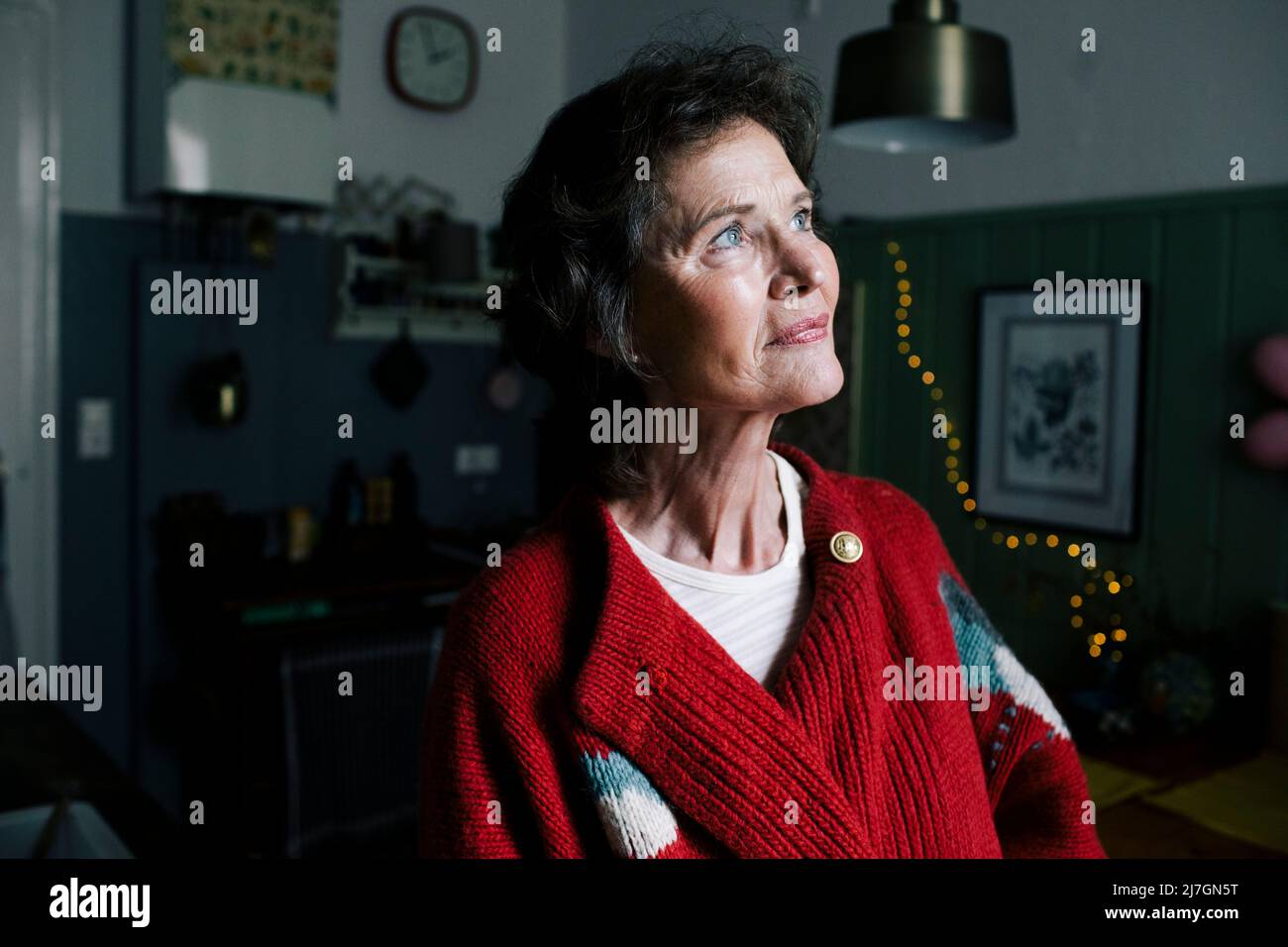 Ältere Frau im Ruhestand, die aufschaut, während sie tagsüber zu Hause träumt Stockfoto