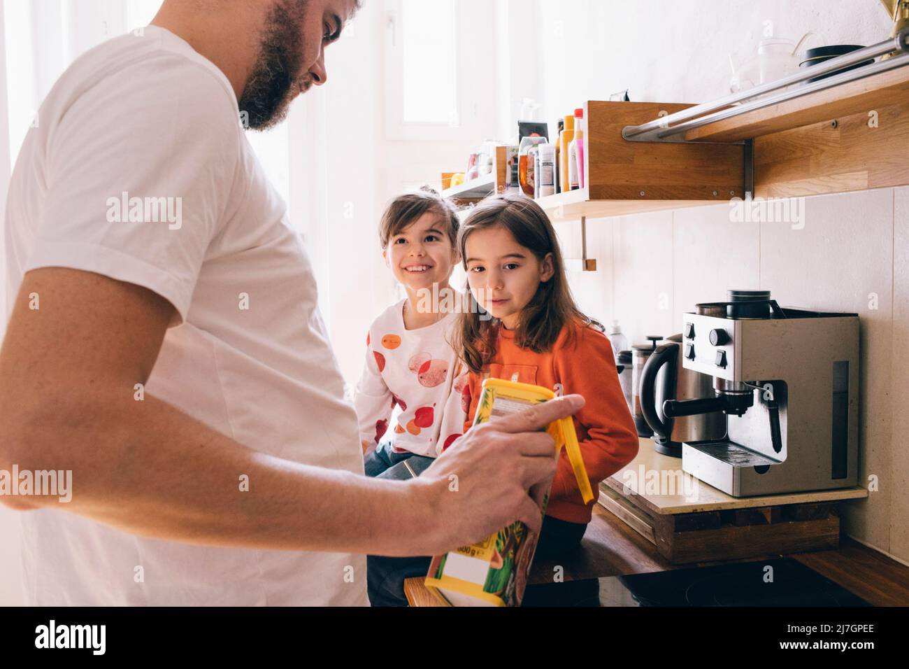 Zwillingsgeschwister sehen Vater, der in der Küche ein Getränk ausgießt Stockfoto