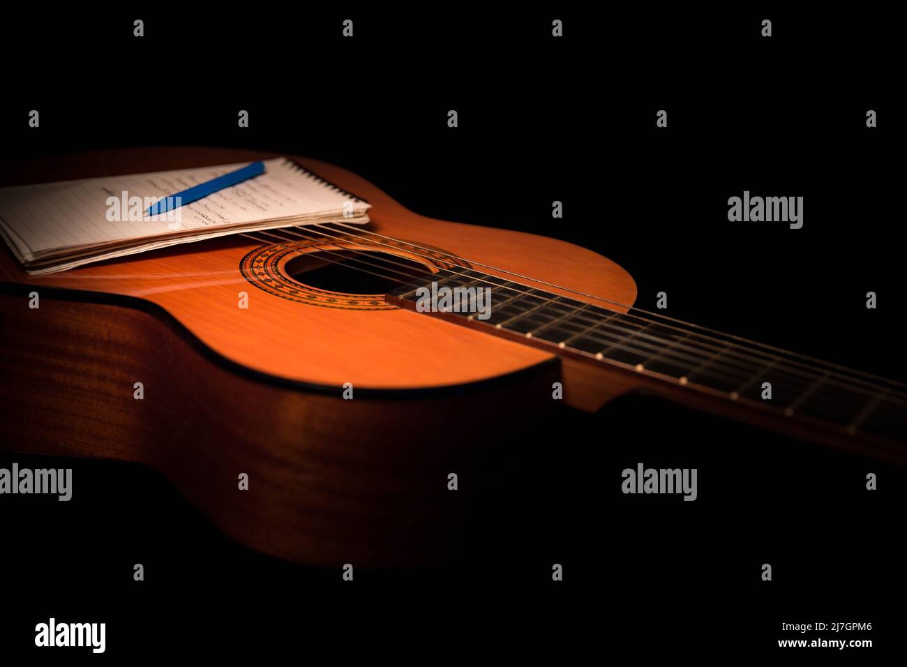 Akustikgitarrenkörper mit klassischer spanischer Gitarre mit Schreibblock und Stift-Nahaufnahme auf schwarzem Hintergrund Stockfoto