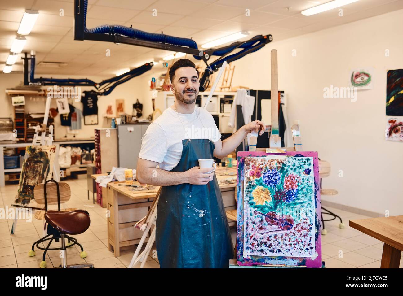 Porträt eines selbstbewussten männlichen Künstlers, der an einer Staffelei mit Malerei in der Kunstklasse steht Stockfoto