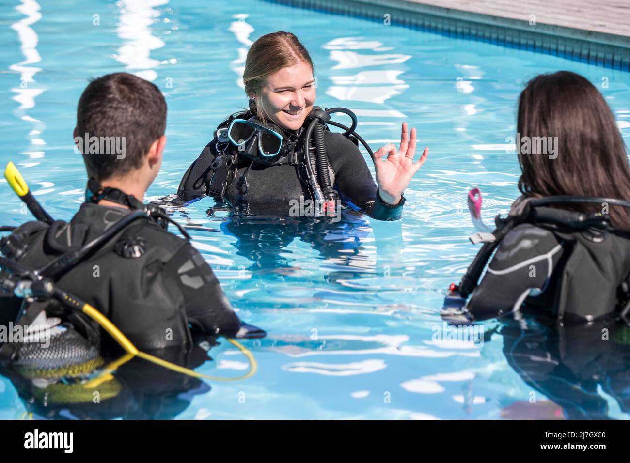 Tauchtraining im Pool mit einem Ausbilder, der zwei Schülern das OK-Zeichen zeigt Stockfoto