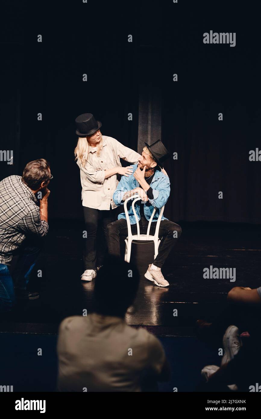 Die ganze Länge der Schauspielerin probt mit einem Mann, der auf dem Stuhl sitzt, während er auf der Bühne probt Stockfoto