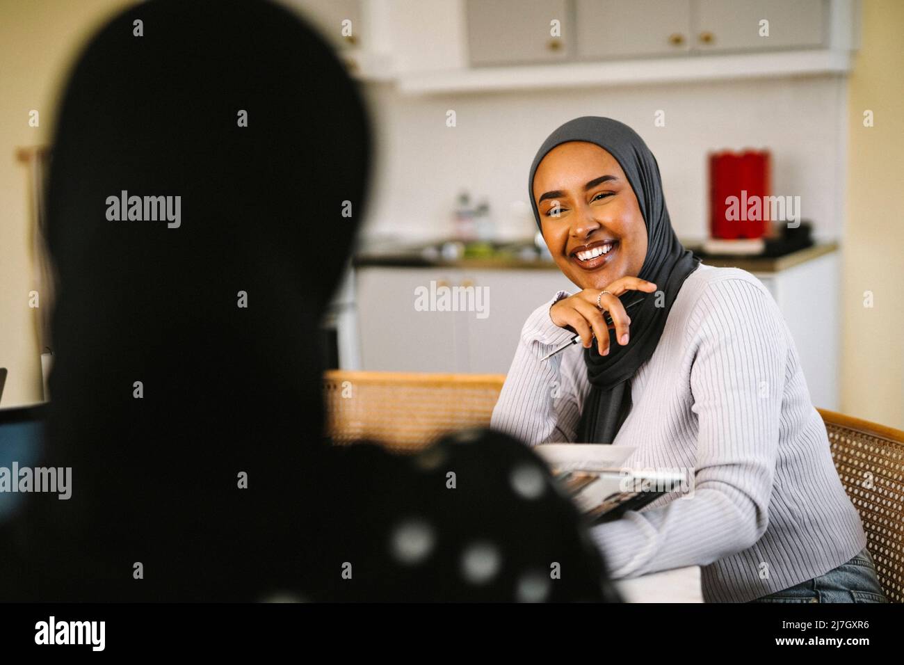 Glückliche junge Frau mit Hijab im Gespräch mit einem Freund zu Hause Stockfoto