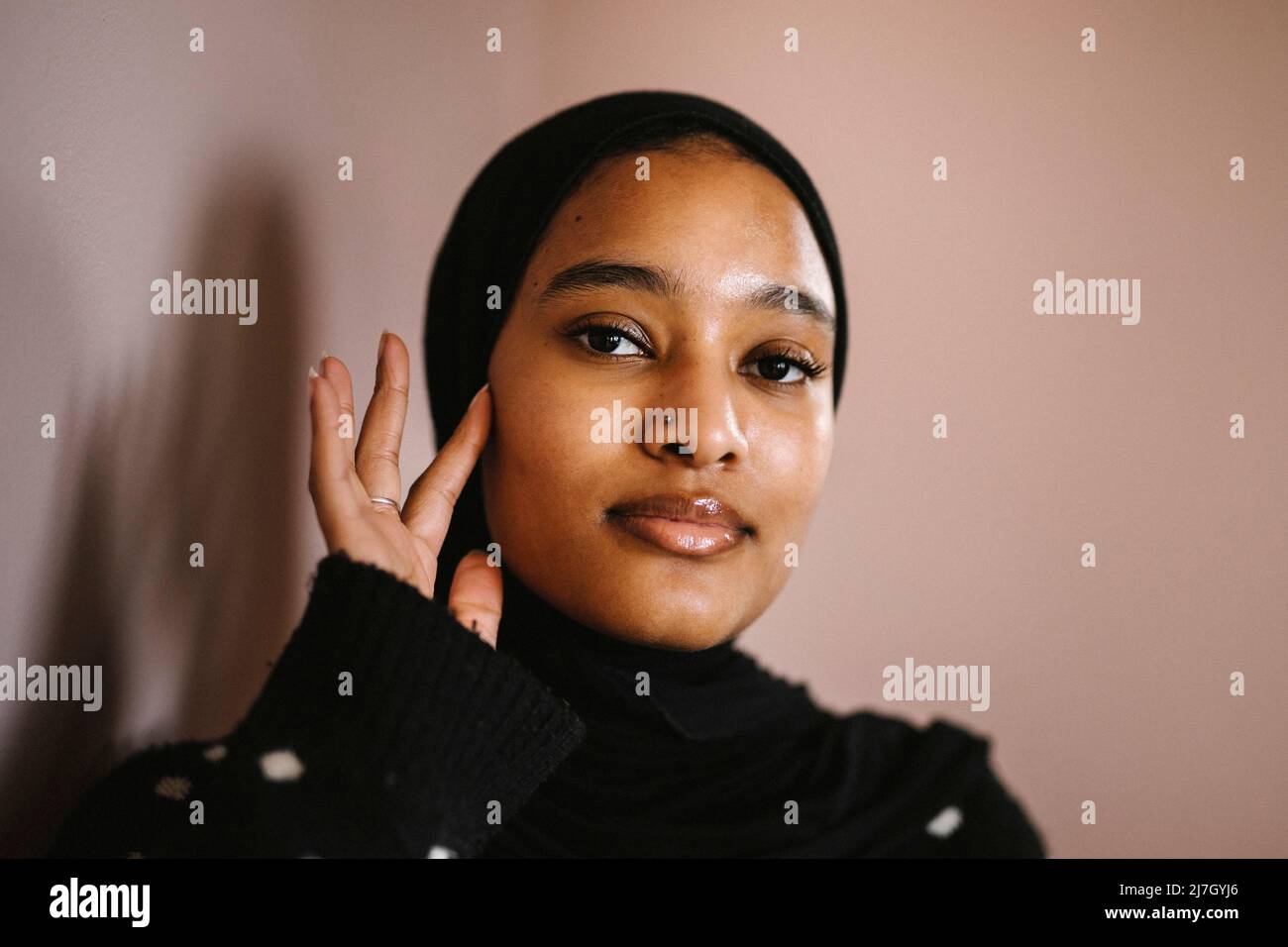 Junge Frau berührt Gesicht vor Pfirsich Hintergrund Stockfoto