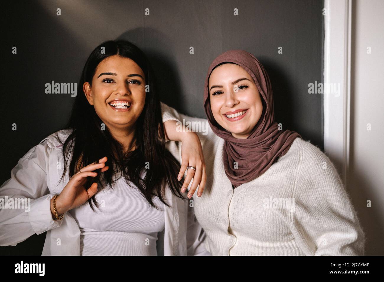 Glückliche junge Frauen, die zu Hause vor der Wand stehen Stockfoto