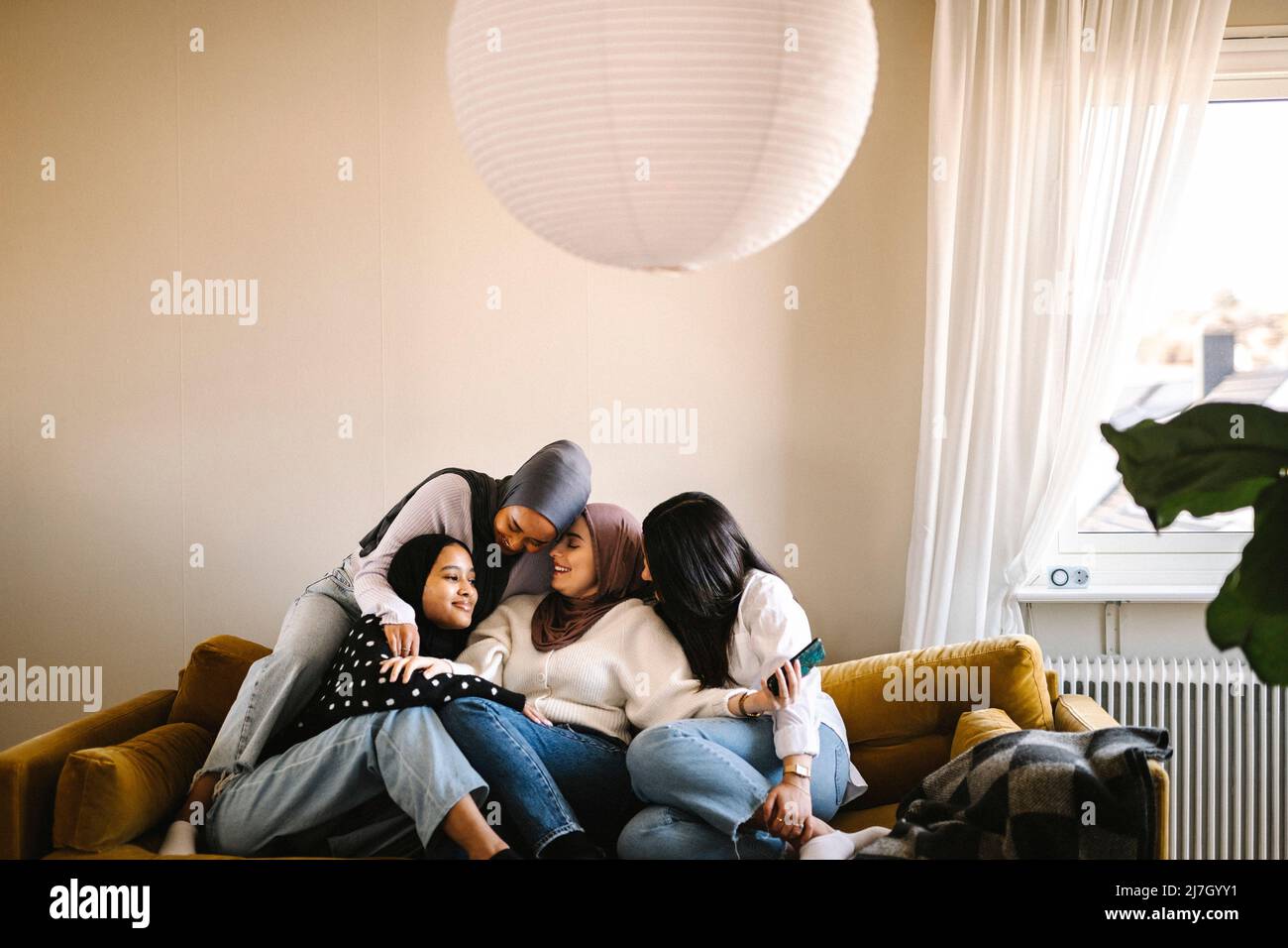 Lächelnde junge Frau umarmt sich gegenseitig auf dem Sofa im Wohnzimmer zu Hause sitzen Stockfoto