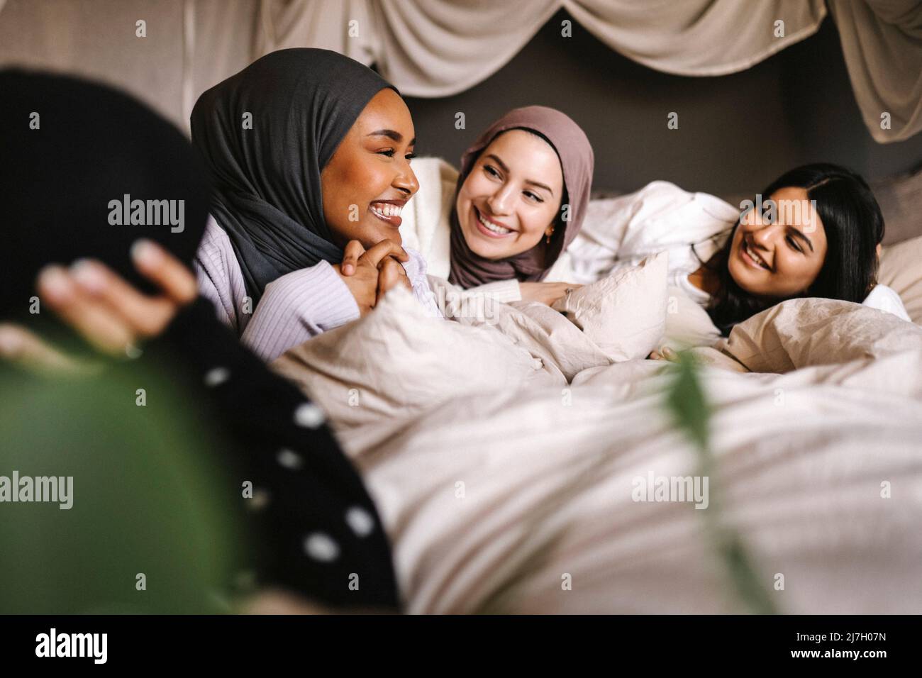 Glückliche junge Frauen in Hijabs, die zu Hause lächelnde Freundin auf dem Bett betrachten Stockfoto