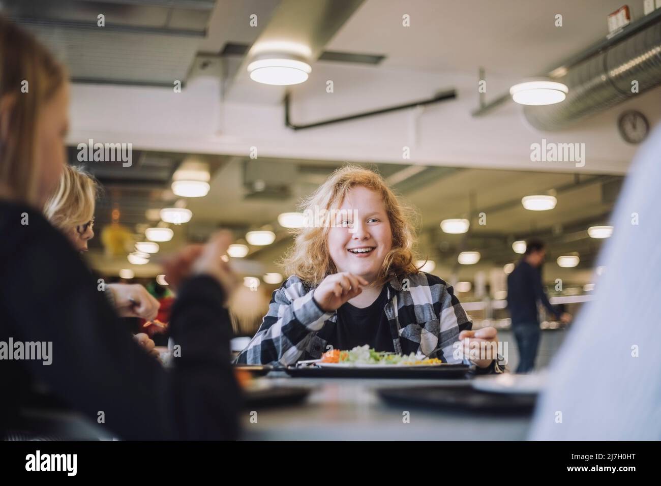 Lächelnder Junge mit Freunden während der Mittagspause in der Cafeteria in der Schule Stockfoto