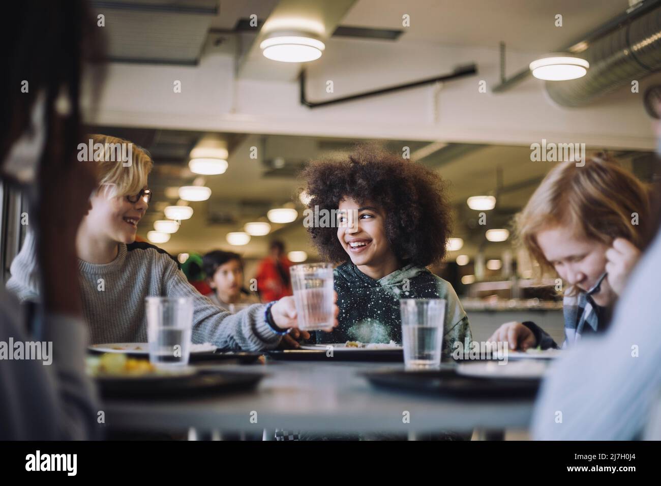 Junge, der während der Mittagspause in der Schule Glas an einen Freund übergibt Stockfoto