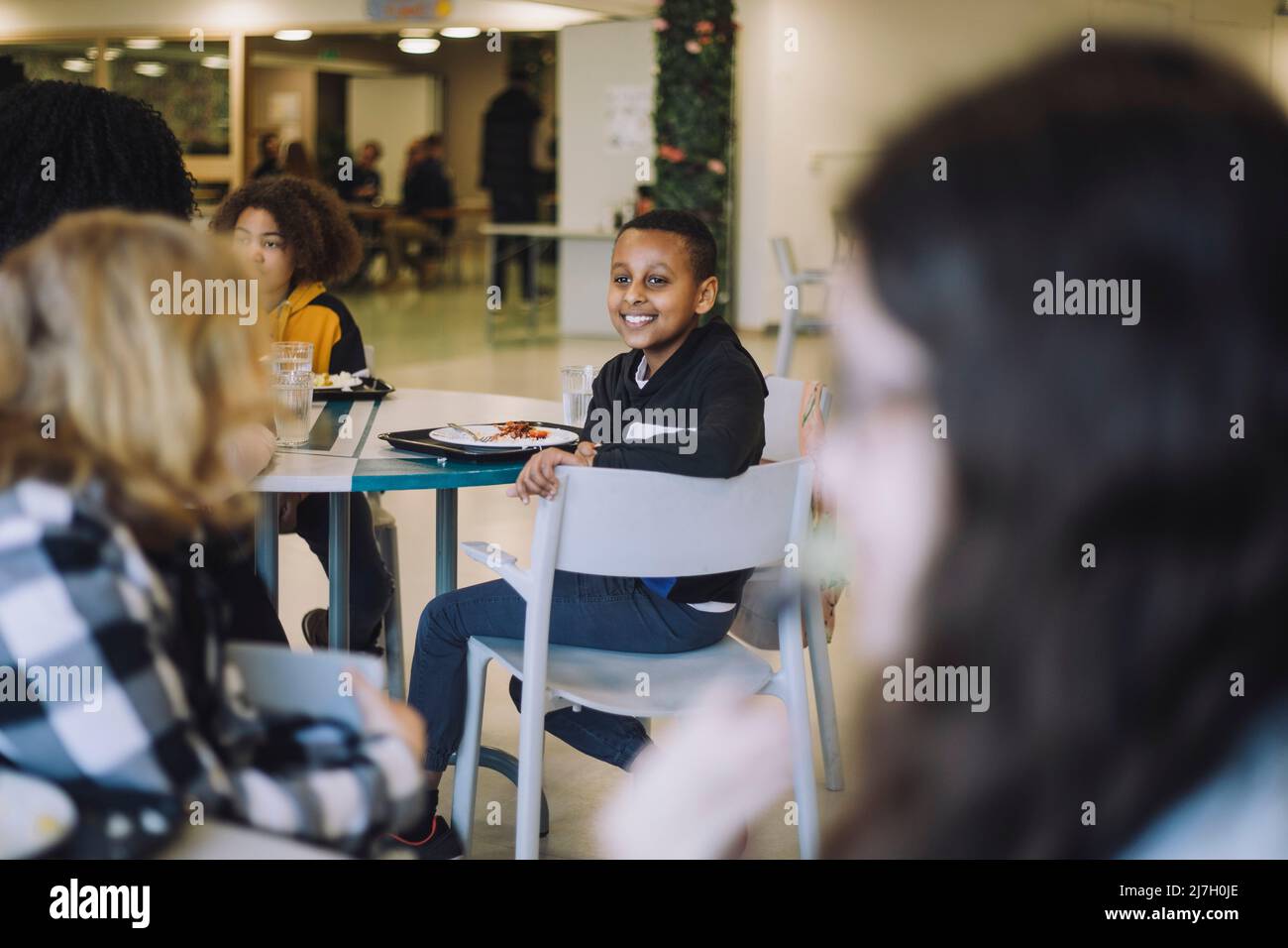 Seitenansicht des Jungen, der während der Mittagspause in der Cafeteria in der Schule auf dem Stuhl sitzt Stockfoto