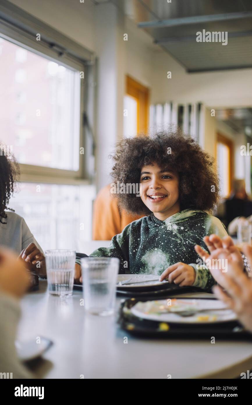 Lächelndes afro Mädchen, das während der Mittagspause in der Schule am Tisch sitzt Stockfoto