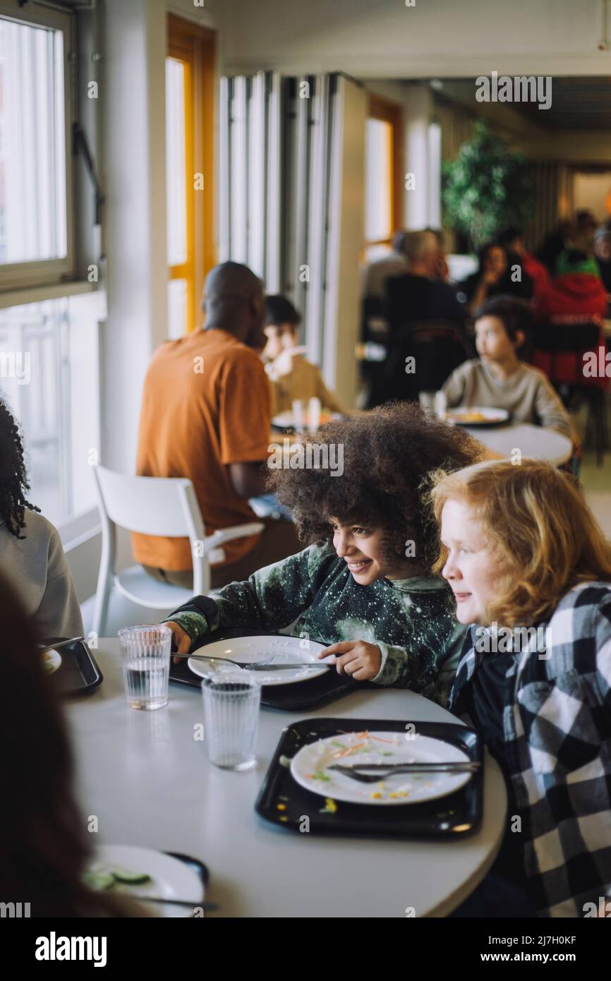 Neugierige Freunde, die während der Mittagspause in der Schulkantine am Tisch sitzen Stockfoto