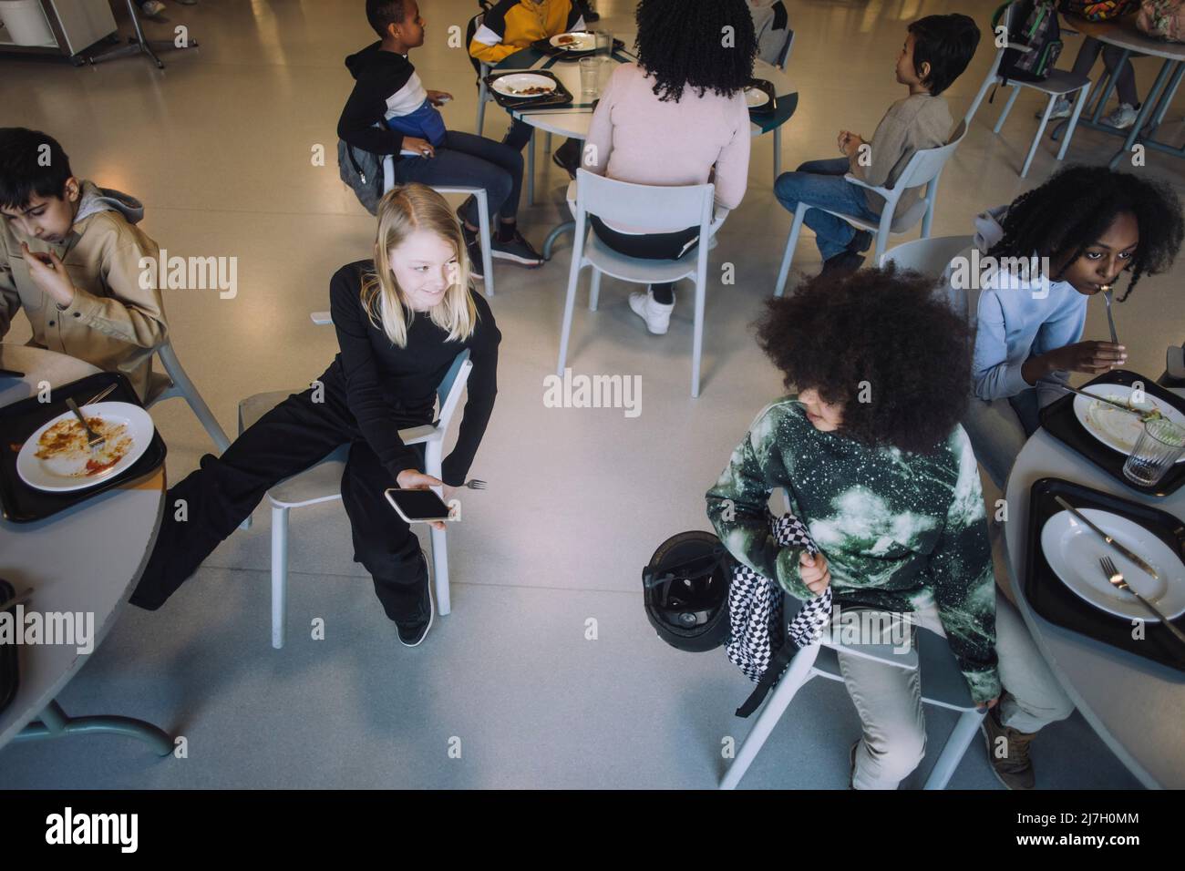 Mädchen teilt Smartphone mit Freund, der während der Mittagspause in der Cafeteria am Tisch sitzt Stockfoto