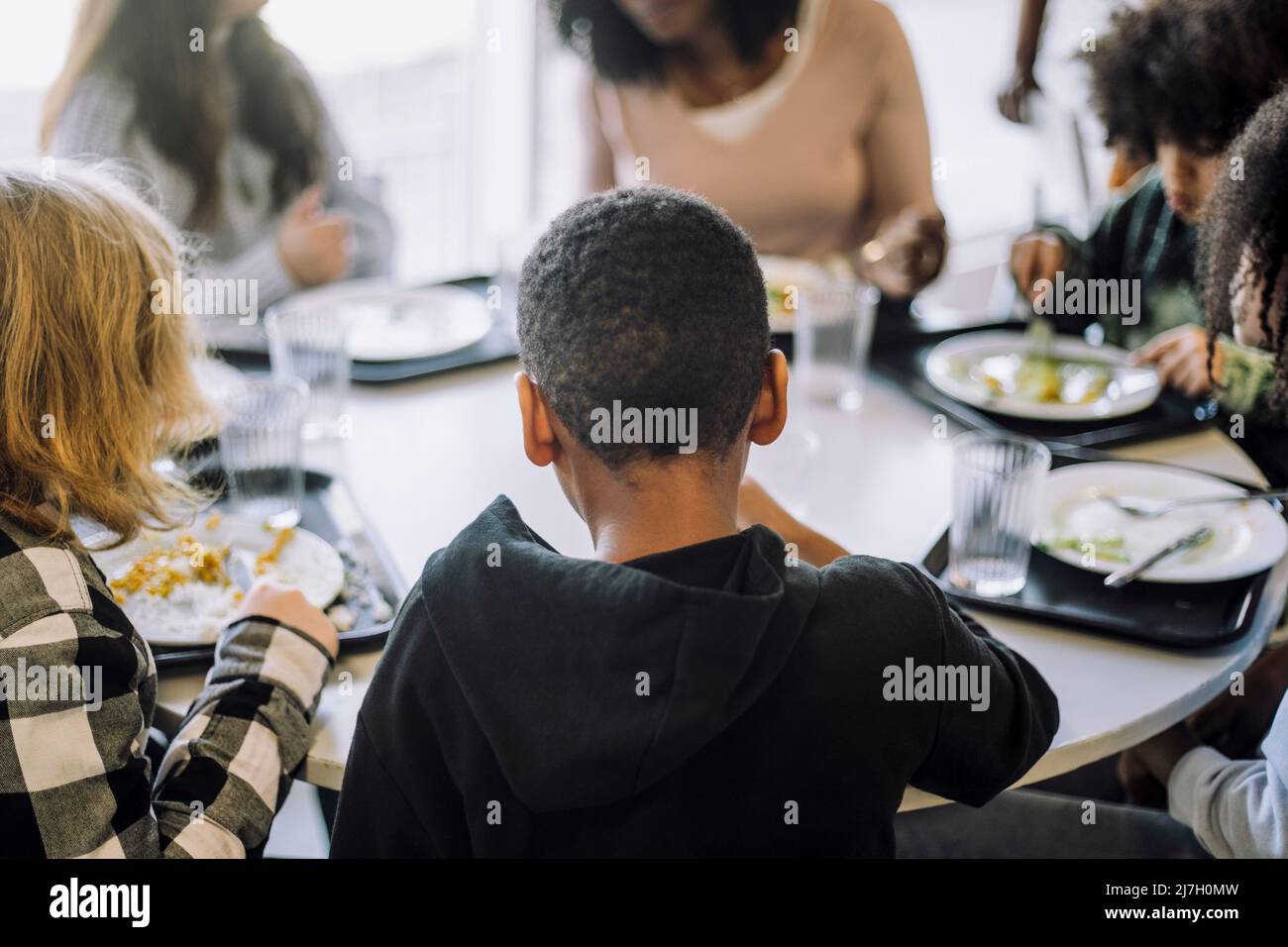 Rückansicht des Jungen, der mit Freunden am Tisch in der Cafeteria sitzt Stockfoto