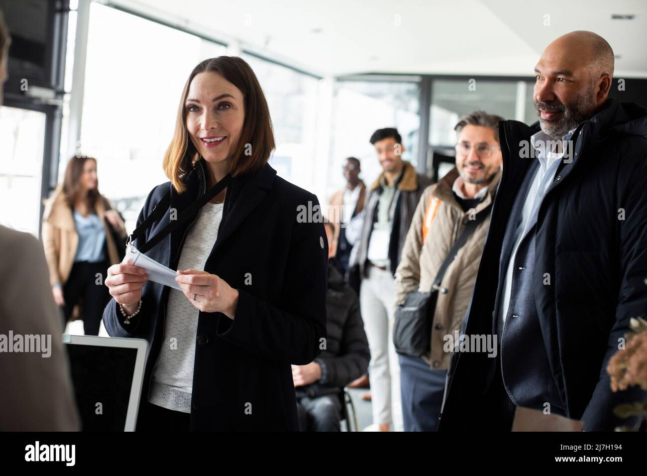 Lächelnde Geschäftsfrau mit Personalausweis und Blick auf die Rezeptionistin im Konferenzzentrum Stockfoto