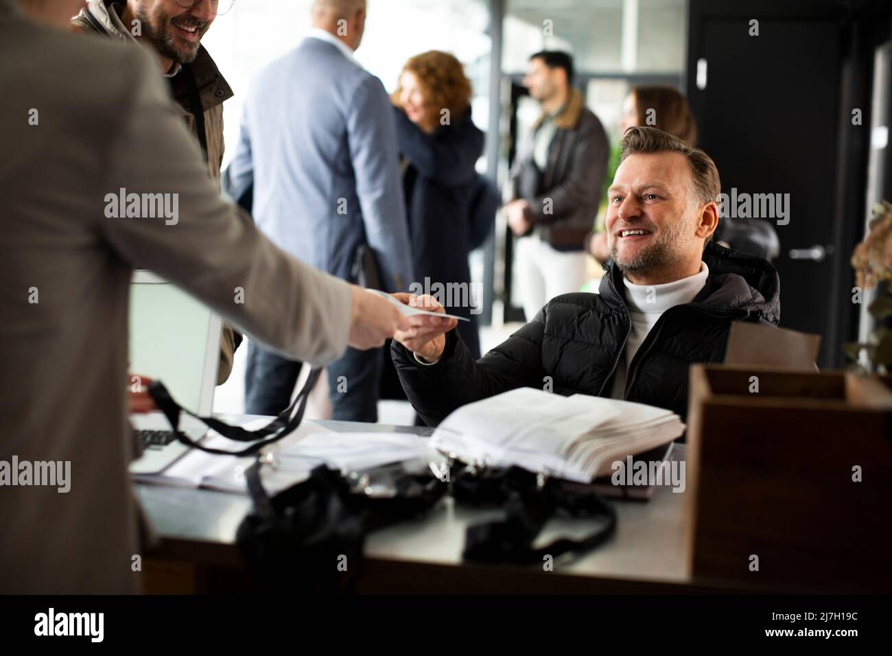 Lächelnder behinderter Geschäftsmann, der am Schalter der Rezeption einen Personalausweis entgegennimmt Stockfoto