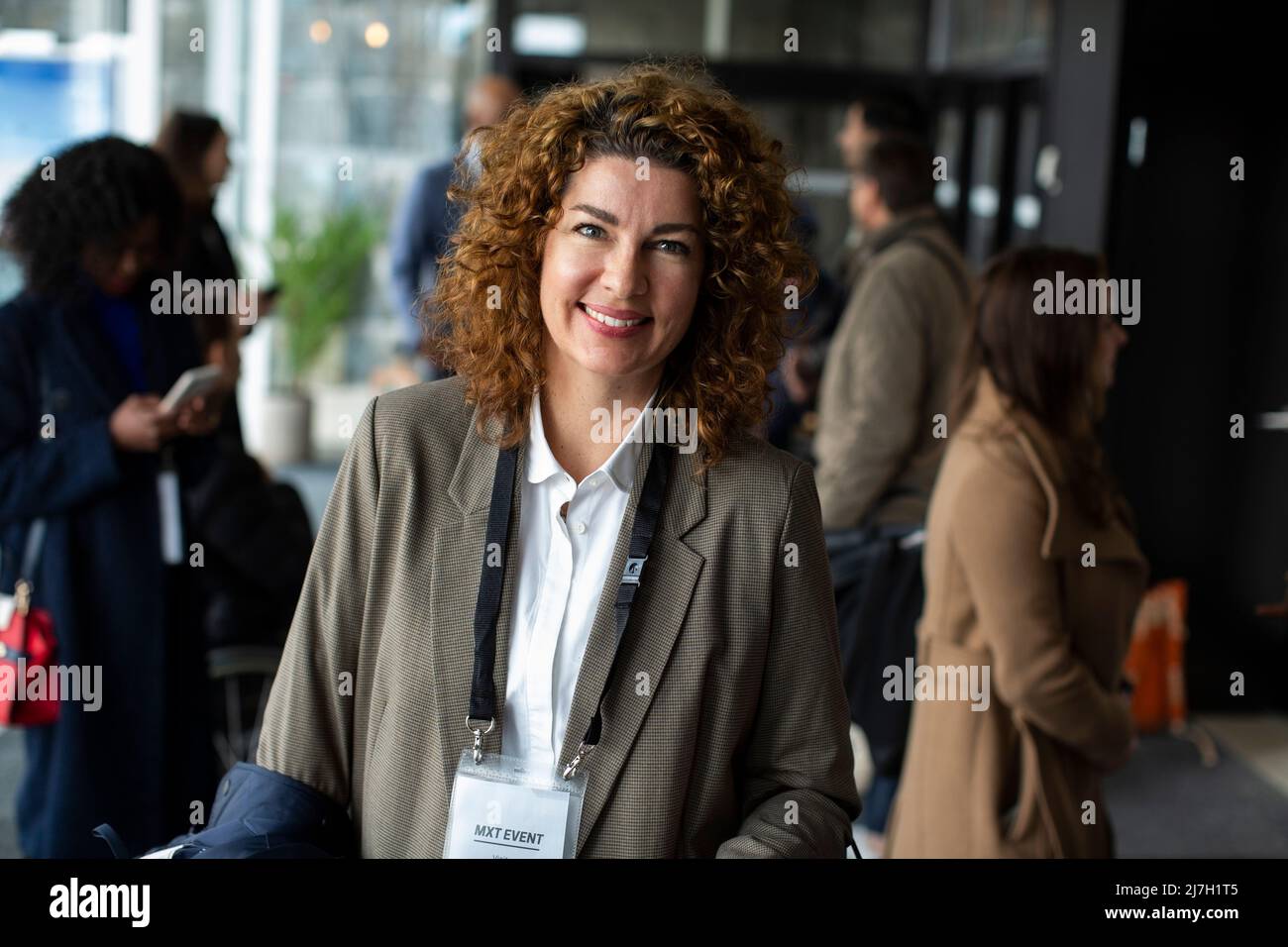 Lächelnde Geschäftsfrau mit lockigen braunen Haaren im Konferenzzentrum während des Seminars Stockfoto