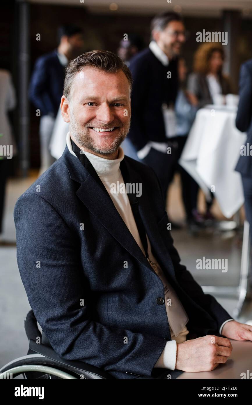 Lächelnder, behinderter Geschäftsmann mit Laptop im Rollstuhl beim Seminar Stockfoto