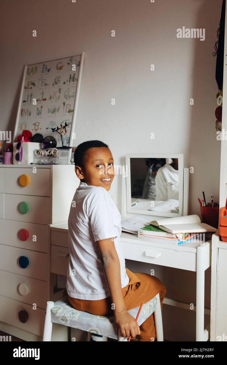 Seitenansicht des Jungen, der über die Schulter schaute, während er am Tisch im Arbeitszimmer saß Stockfoto