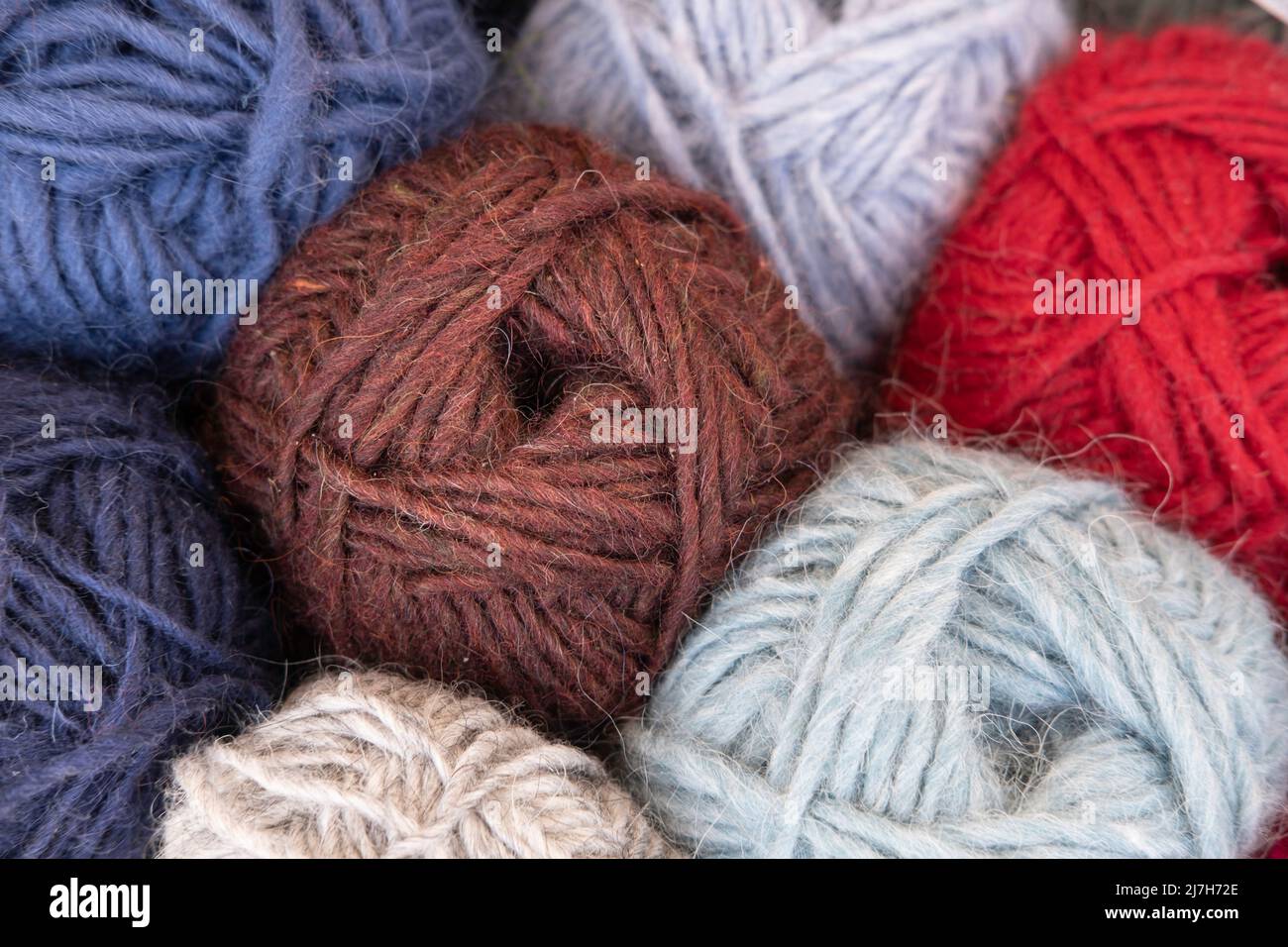 Nahaufnahme von Strickbällen aus Wolle in verschiedenen Farben. Konzentriere dich auf die Fäden des braunen Wollknochens in der Mitte Stockfoto
