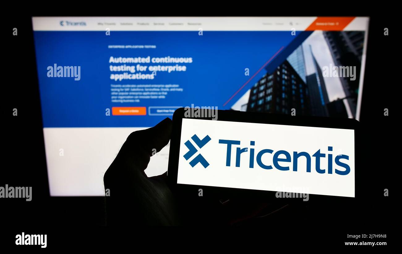Person, die Mobiltelefon mit Logo des österreichischen Softwareunternehmens Tricentis GmbH auf dem Bildschirm vor der Business-Webseite hält. Konzentrieren Sie sich auf die Telefonanzeige. Stockfoto